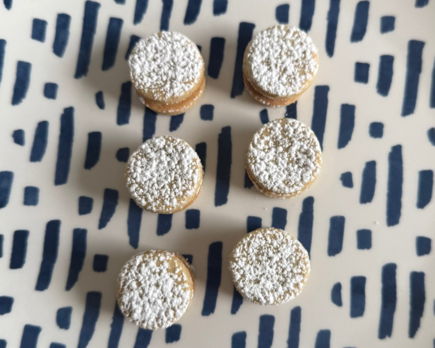 Six small round cookies with powdered sugar on a plate with a blue abstract pattern